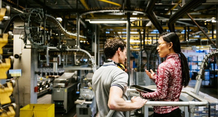 a young white male business man speaking to a female Chinese factory manager in a manufacturing factory